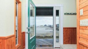 Une porte en bois qui donne sur une terrasse offrant une vue sur une plage et des bâtiments.