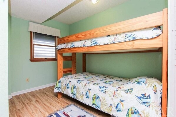 A bunk bed room with a window, a wooden ladder, and a patterned bedspread.