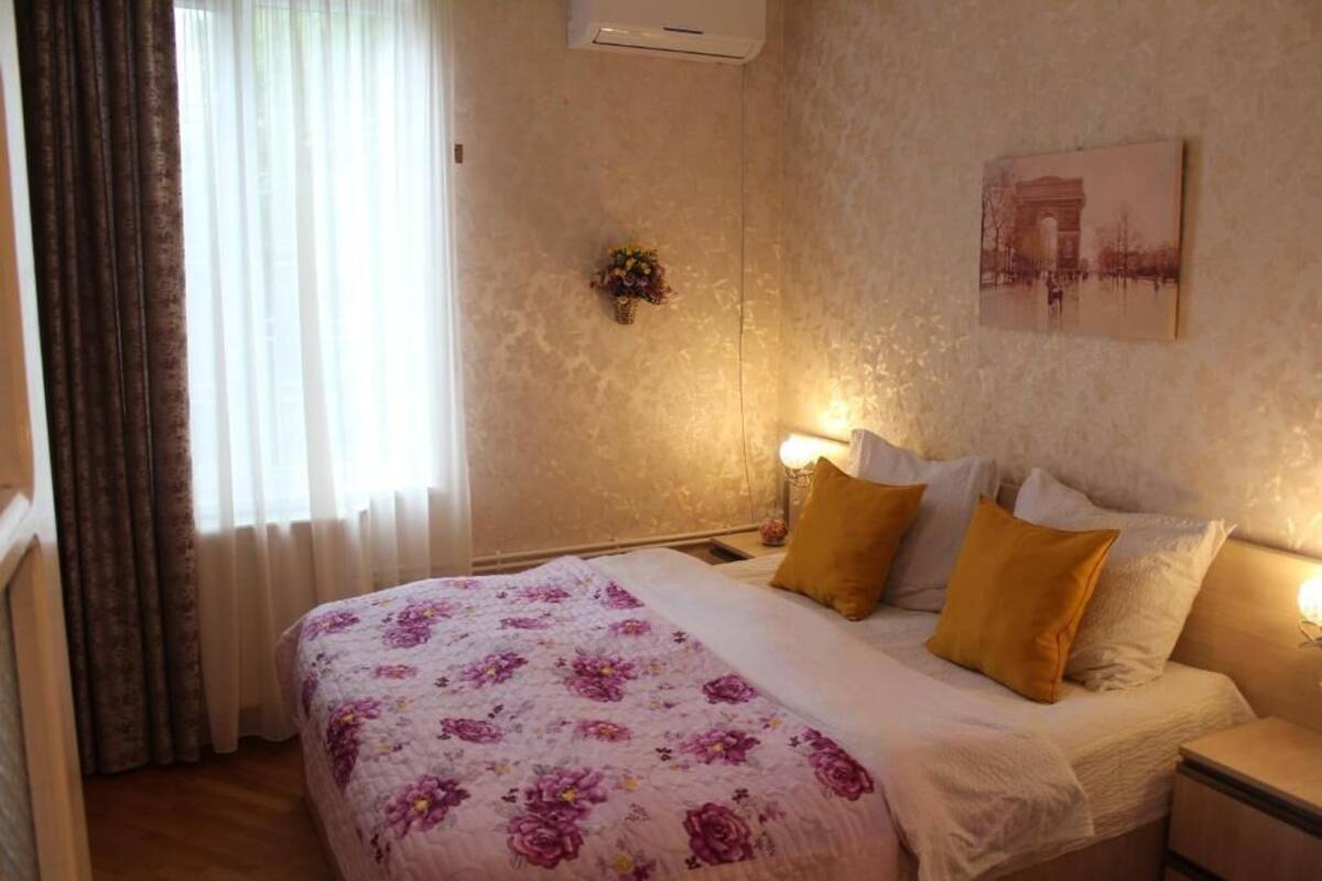 A hotel room with a bed, bedside lamps, a wall-mounted air conditioner, and a framed picture.