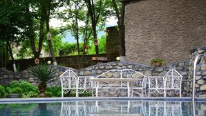 A pool area with a stone wall and a white metal bench. - Guesthouse Lago & Wine Cellar (Lagodekhi)