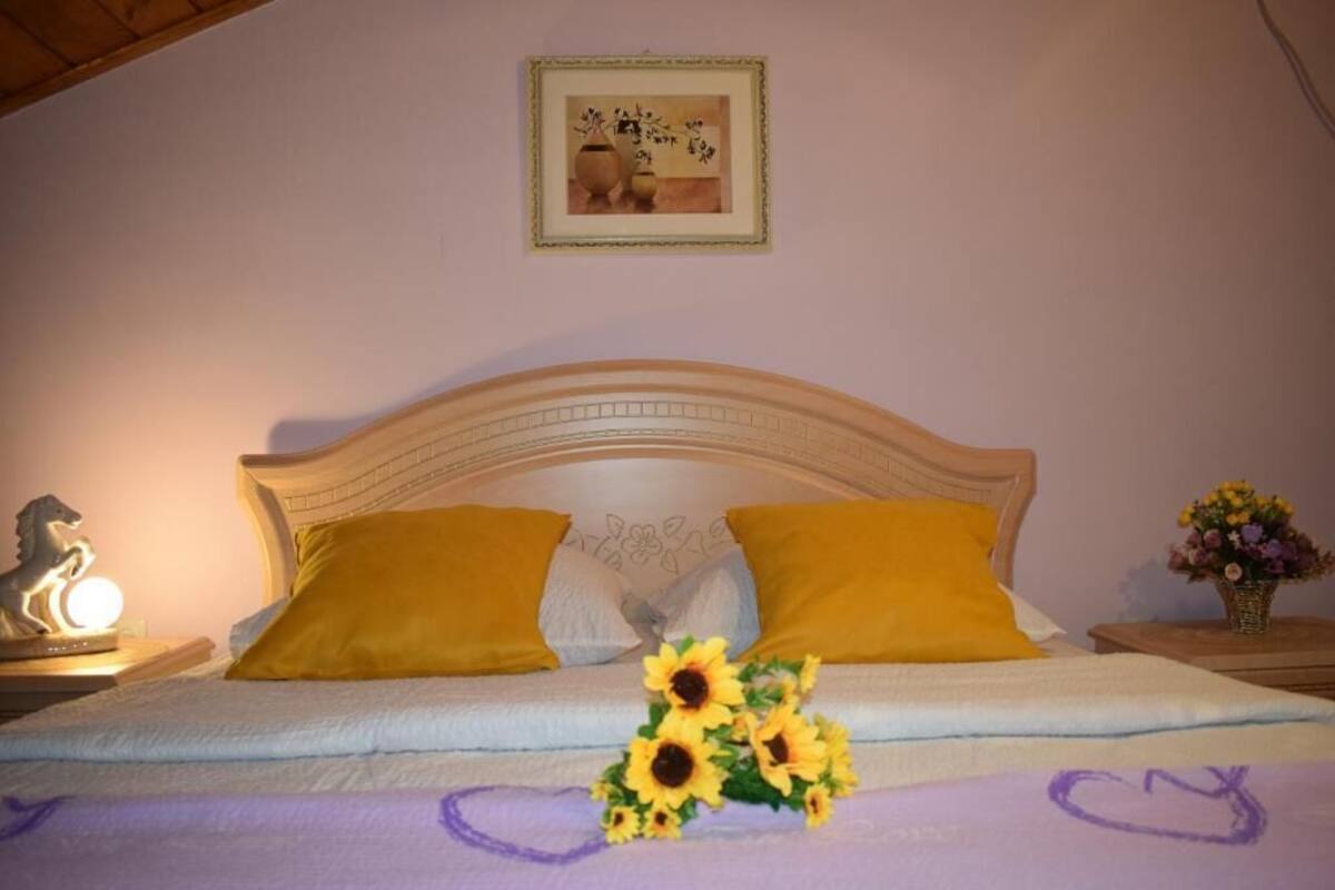 A bedroom with a wooden headboard, two yellow pillows, a bedside table with a lamp, and a vase with flowers.
