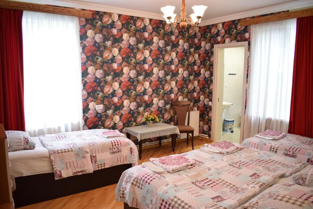 A room with two beds, a table with a vase of flowers, and a chair.