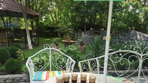 A garden patio with a white metal table and chairs, surrounded by lush greenery and stone walls. - Guesthouse Lago & Wine Cellar (Lagodekhi)
