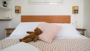 Una cama con un osito de peluche, una almohada rosa y una colcha estampada con motivos florales.