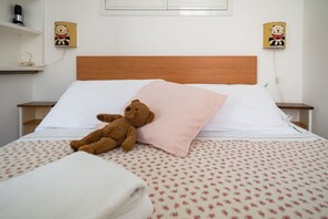A bed with a teddy bear, a pink pillow, and a floral-patterned bedspread.