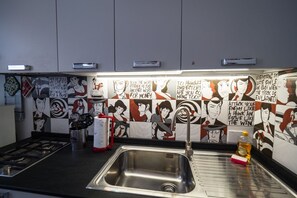 A kitchen with a stainless steel sink, a gas stove, and a tiled backsplash with cartoon characters. - Nonna Rosetta Traditional Studio (Vernazza)