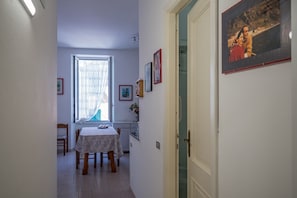 A narrow hallway with a dining table and chairs, a window with curtains, and framed pictures on the walls.