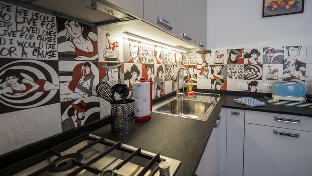 Una cocina con estufa a gas, un lavamanos y un salpicadero de azulejos con ilustraciones.