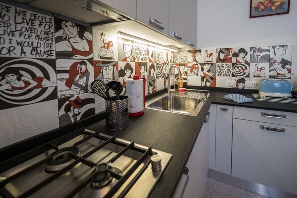 A kitchen with a gas stove, a sink, and a tiled backsplash with illustrations.