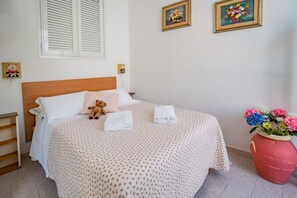 A neatly made bed with a teddy bear, a vase of flowers, and two framed pictures on the wall.