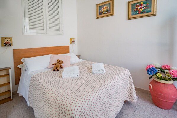 A neatly made bed with a teddy bear, a vase of flowers, and two framed pictures on the wall. - Nonna Rosetta Traditional Studio (Vernazza)