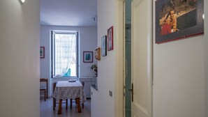 Un pasillo estrecho con una mesa de comedor y sillas, una ventana con cortinas y cuadros en las paredes.