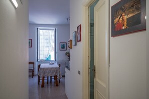 A narrow hallway with a dining table and chairs, a window with curtains, and framed pictures on the walls.