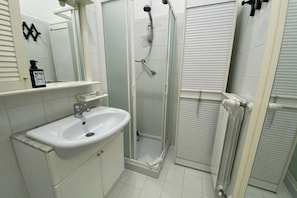 A bathroom with a white sink, mirror, shower, and radiator.