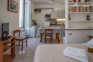 A compact room with a bed, a desk, a chair, a TV, a bookshelf, and a kitchenette. - Nonna Rosetta Traditional Studio (Vernazza)