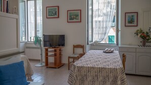 Una sala de estar con sofá, televisión, mesa de comedor y ventana con cortinas.