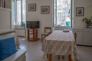 A living room with a sofa, a TV, a dining table, and a window with curtains.