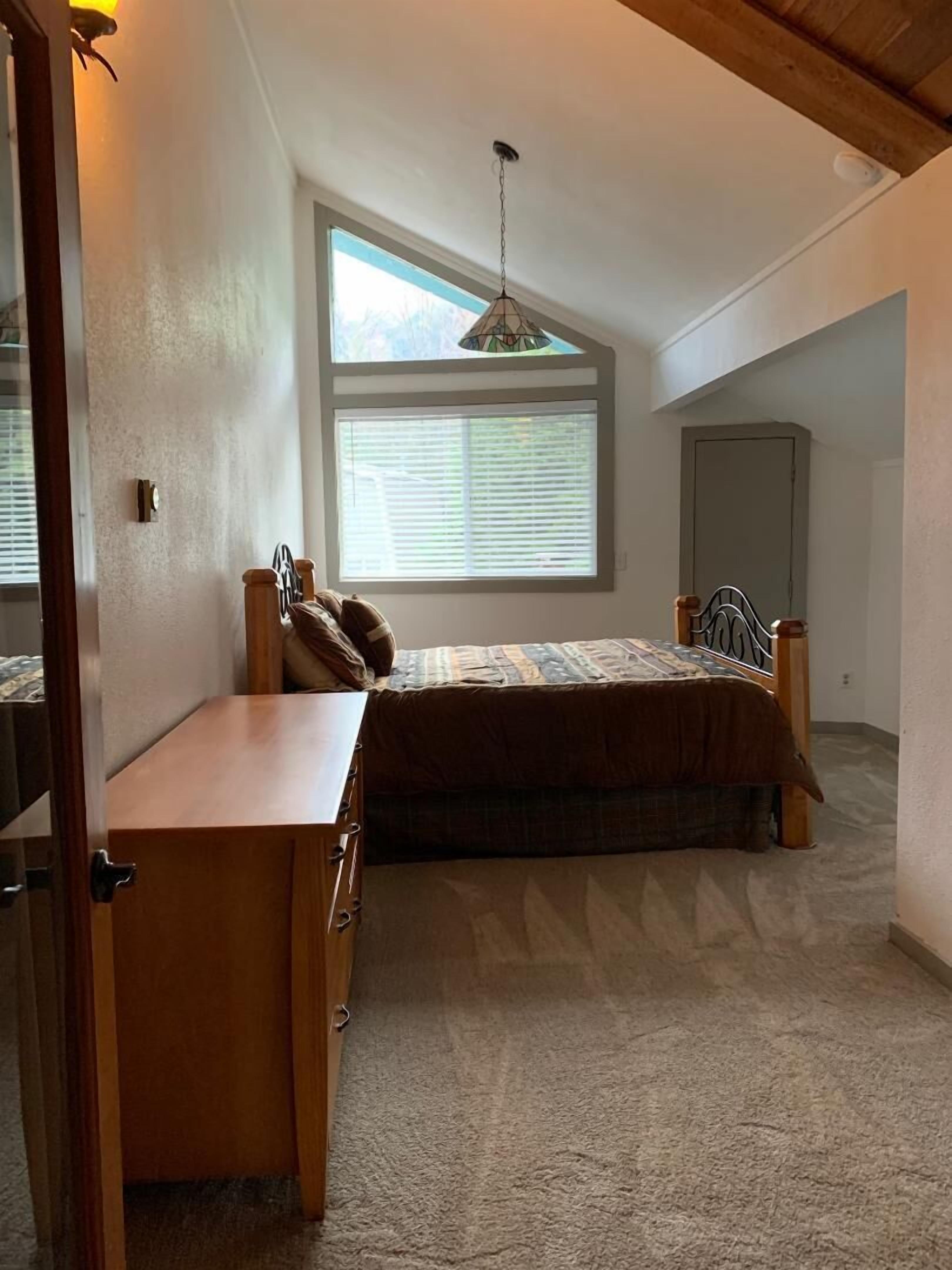 A bedroom with a bed, a desk, and a window.