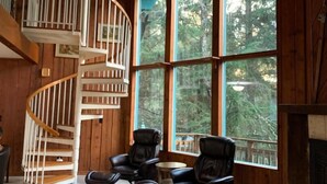 A wooden interior with a spiral staircase, large windows, and leather chairs. - Stellar Blue Chalet - Sleeps 6+. Pets on approval. Near Alyeska Ski Resort (Girdwood)