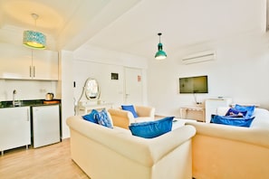 A modern living room with a sofa set, a small kitchen area, and a television. - Nur Suites & Hotels (Kas)