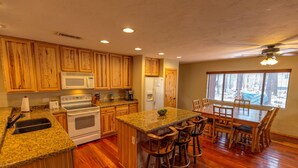 Une cuisine dotée de meubles en bois, d’un plan de travail en granit, d’un four encastré, d’un four à micro-ondes, d’un réfrigérateur et d’un coin repas avec un grand îlot central et des tabourets de bar.