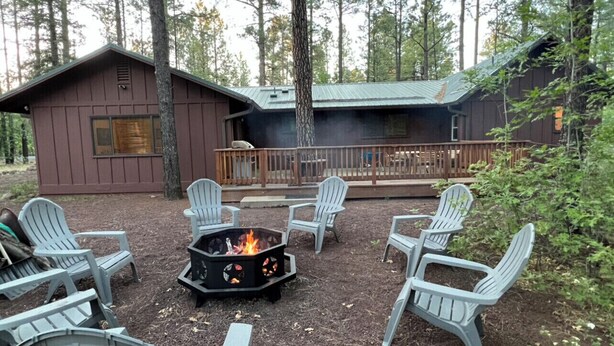 Une cabane dotée d’une terrasse, entourée de fauteuils Adirondack, et avec un foyer central.