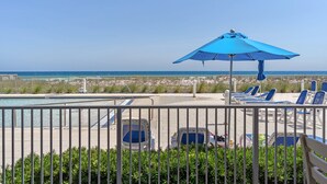 Ein Poolbereich mit Liegestühlen und einem blauen Sonnenschirm mit Blick auf den Strand.