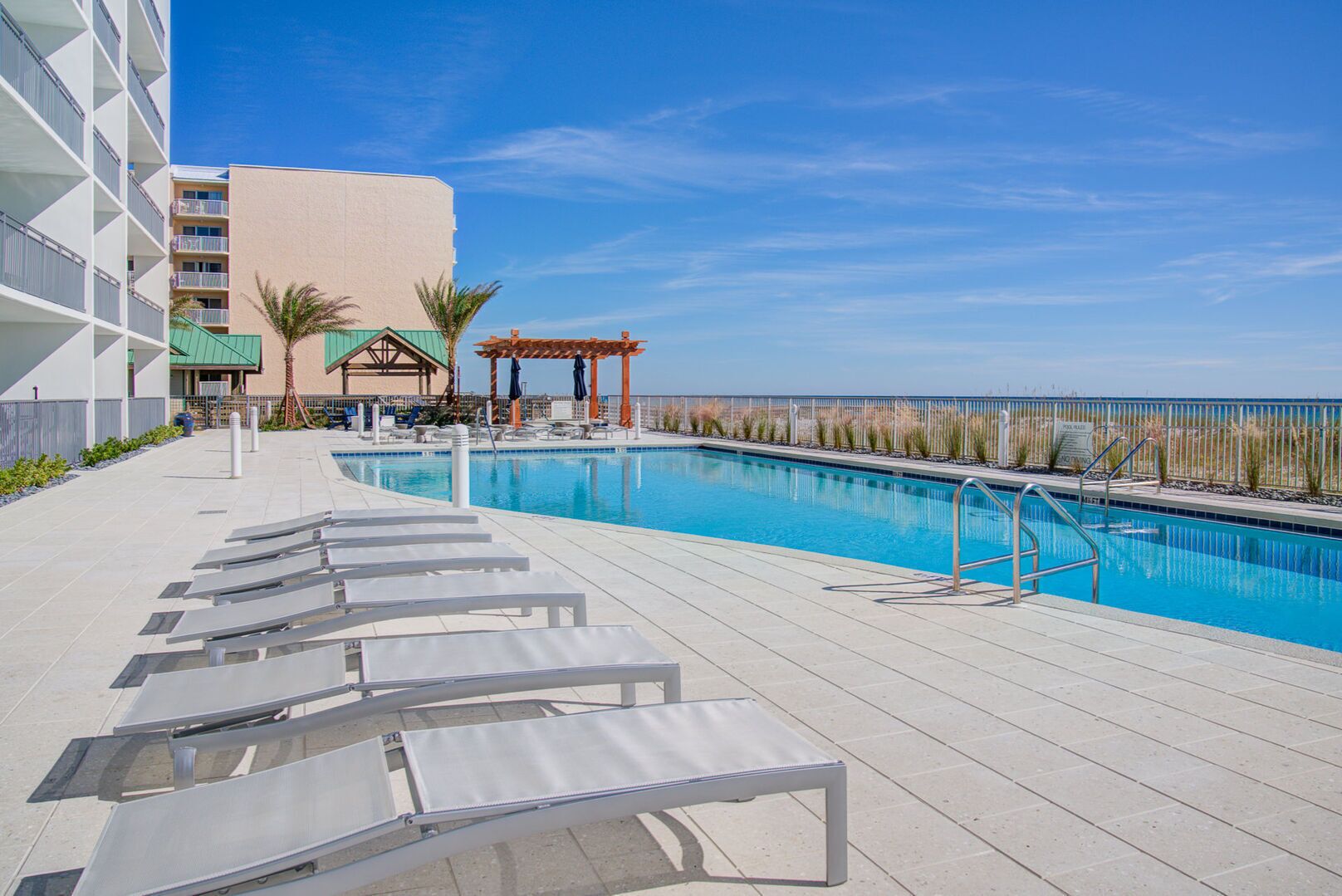 Area piscina con lettini, una pergola e vista sull'oceano.