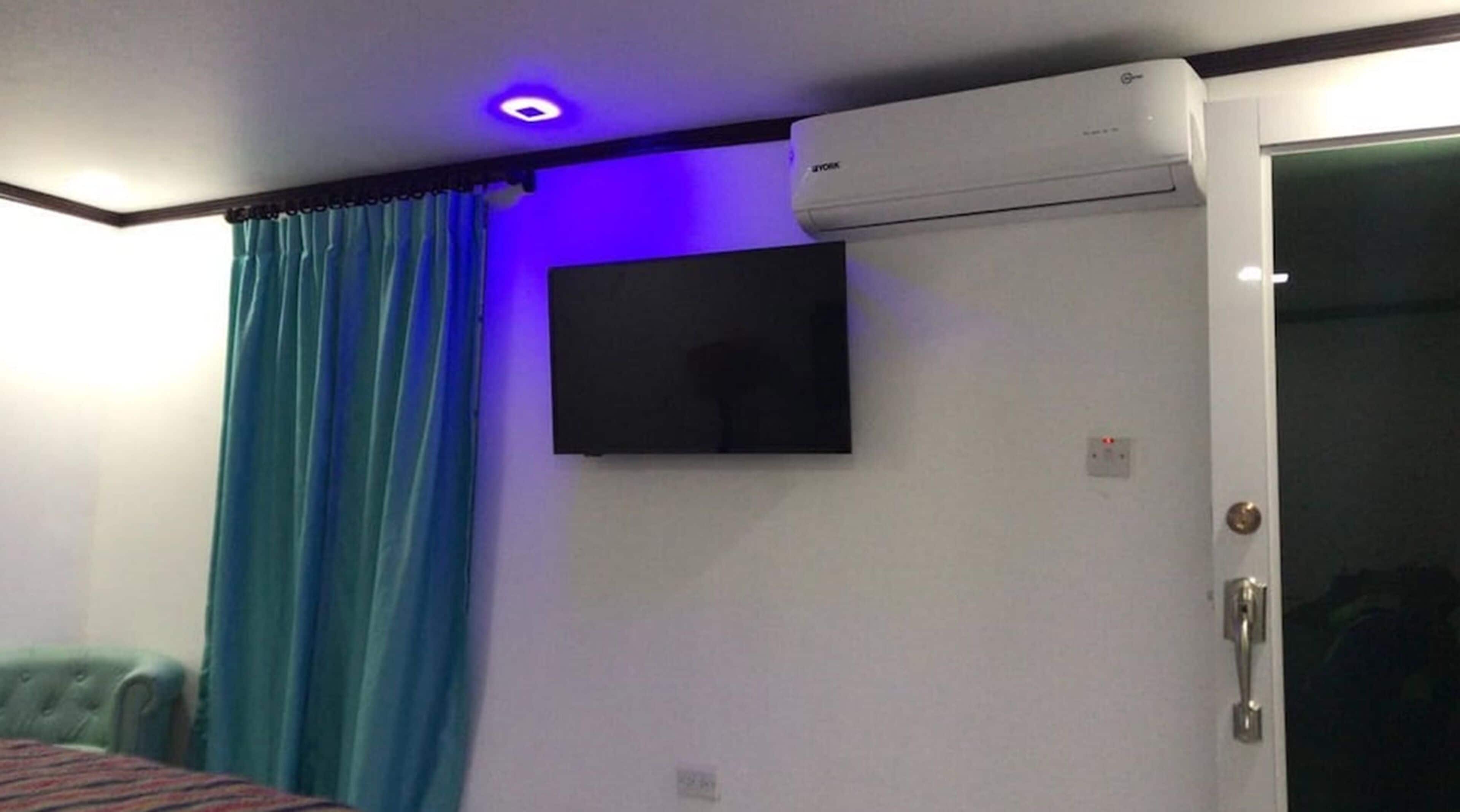 A room with a closed door, a mounted air conditioner, a flat-screen TV on the wall, and a blue curtain.
