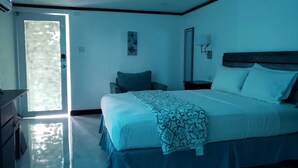 A bedroom with a bed, bedside table, and a window. - Sand and Blue Seas (Negril)