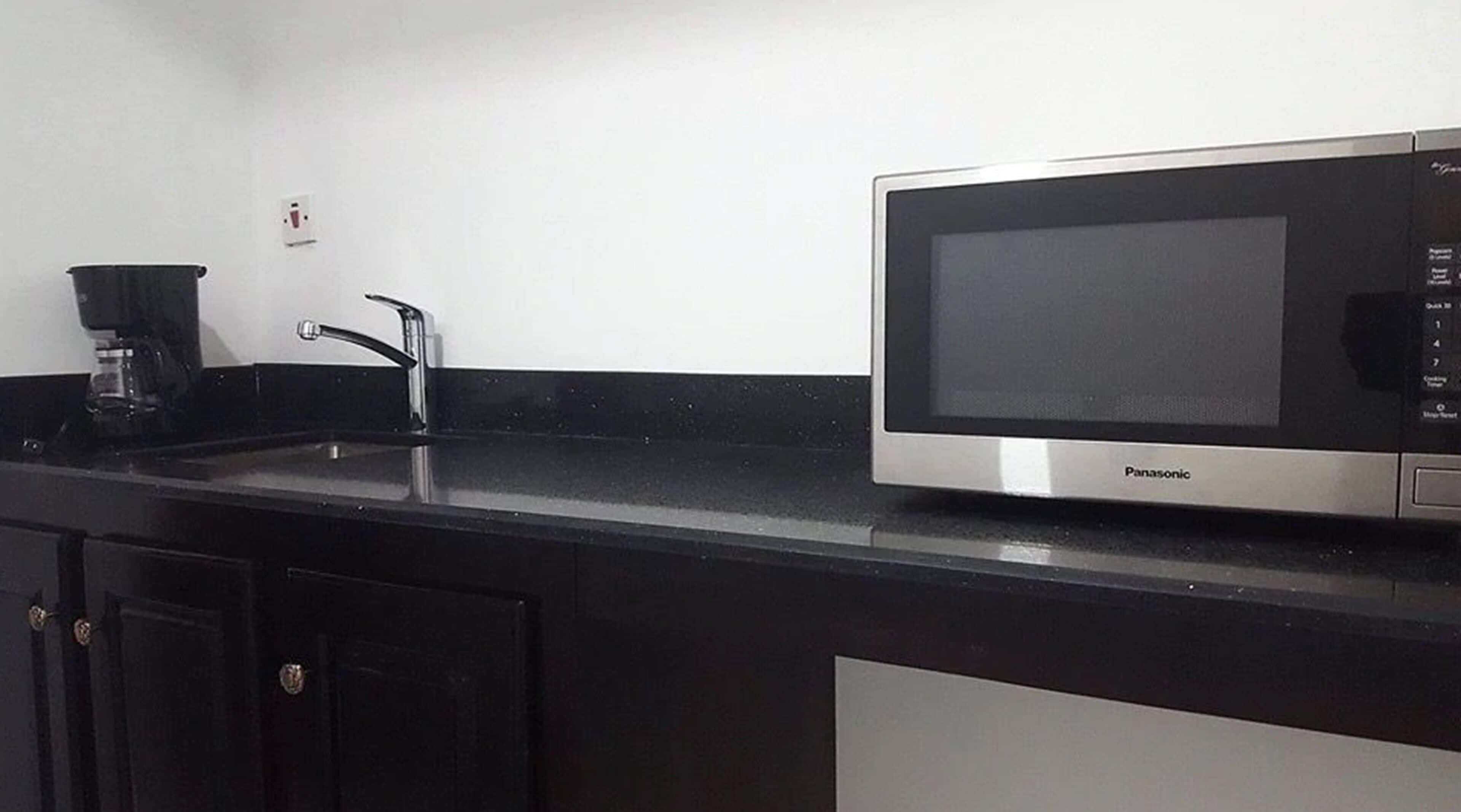 A kitchen with a black countertop, a stainless steel microwave, a coffee maker, and black cabinets.