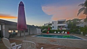 A pool area with lounge chairs and umbrellas, surrounded by buildings and palm trees. - Sand and Blue Seas (Negril)