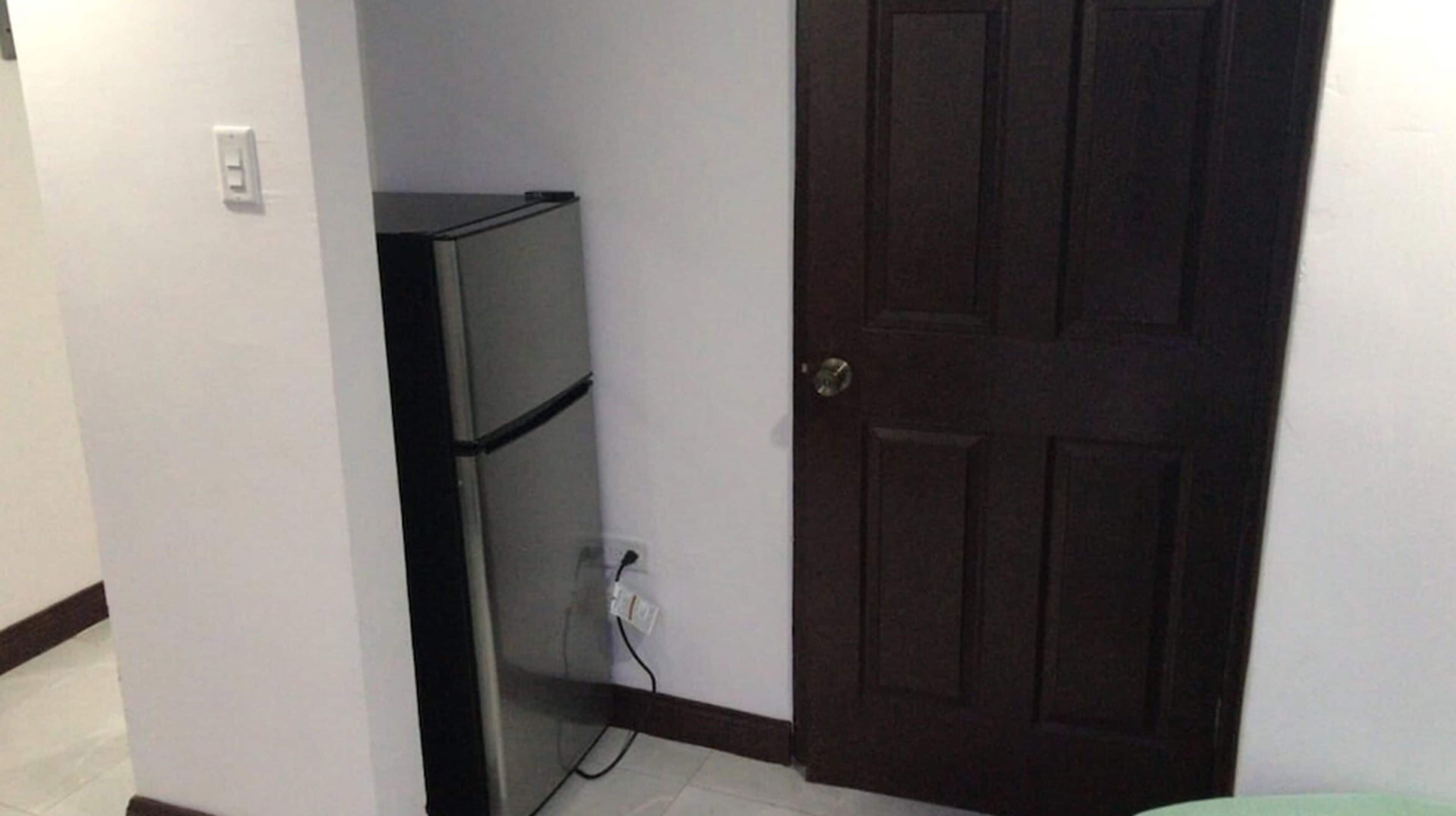 A compact room with a closed door, a small refrigerator, and a power outlet on the wall.