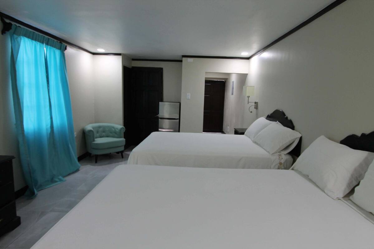 A hotel room with two beds, a chair, a refrigerator, and a door leading to another room.