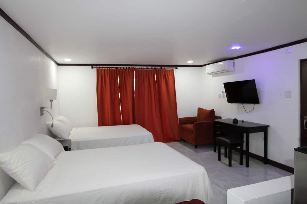 A hotel room with two beds, a desk, a chair, a TV, and a window with red curtains.