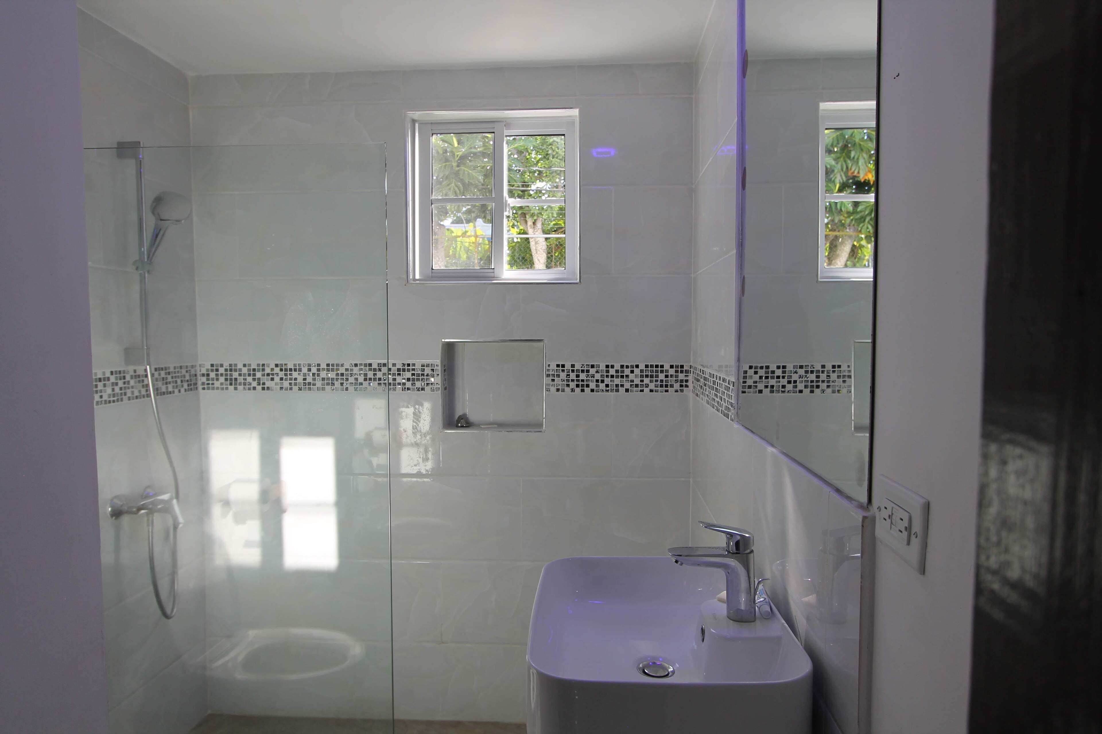A modern bathroom with a glass-enclosed shower, a small window, and a sink with a mirror.