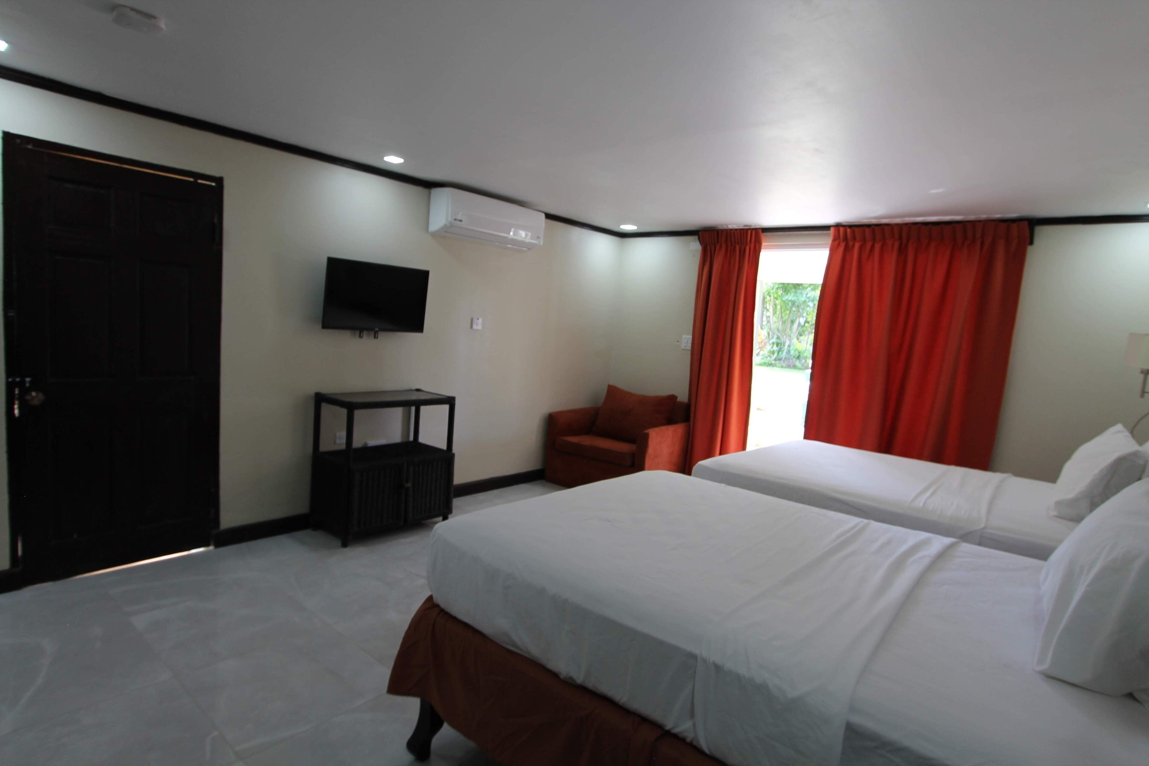 A hotel room with two beds, a TV, an air conditioner, a chair, and a window with curtains.
