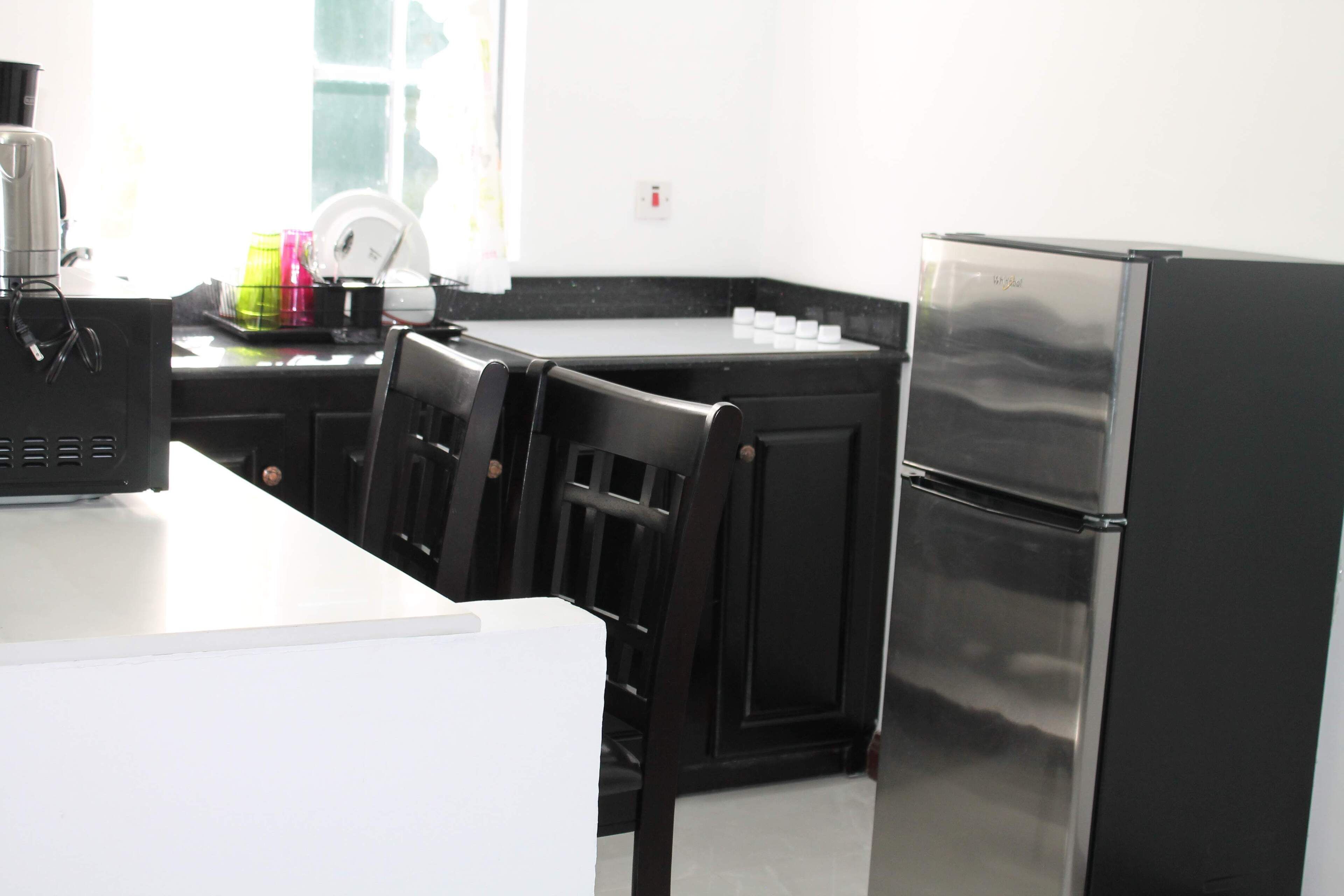 A kitchen with a white countertop, black chairs, a stainless steel refrigerator, and a coffee machine.