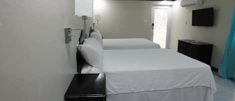 A hotel room with two beds, a bedside table, a TV mounted on the wall, and a window with curtains.