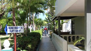 A pathway lined with greenery, a sign for a mini mart and gift shop, and a building with a balcony. - Sand and Blue Seas (Negril)