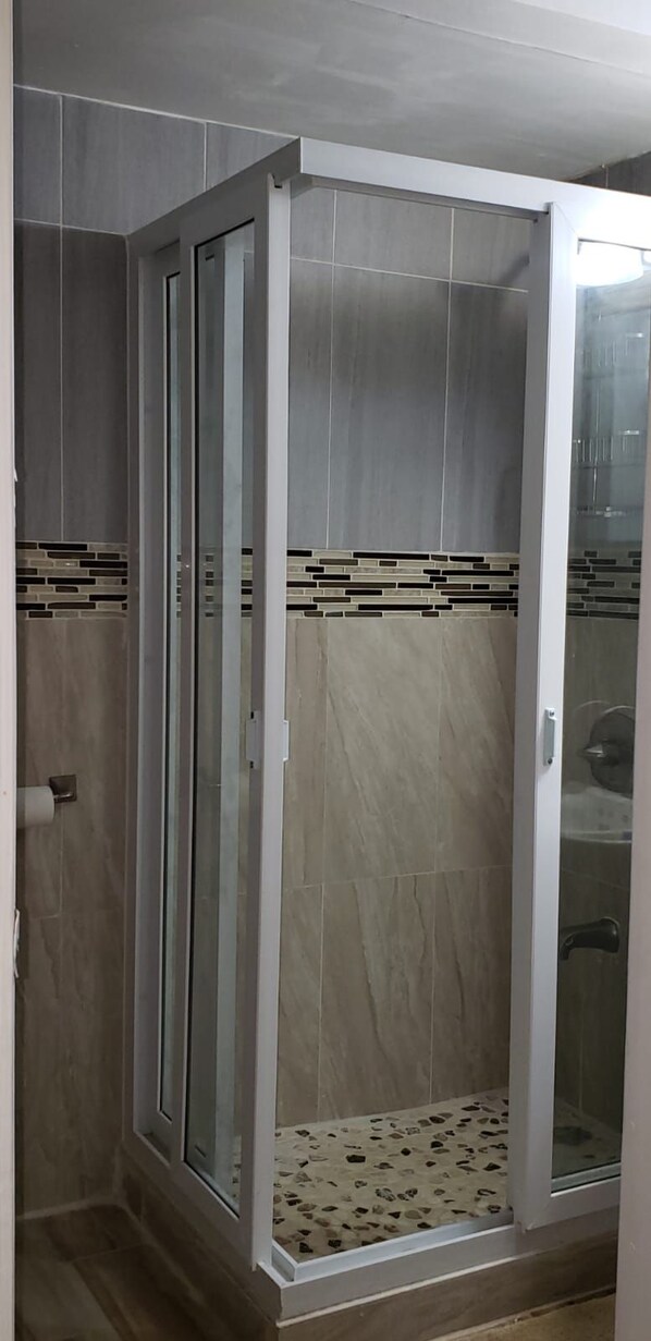 A walk-in shower with a glass door, tiled walls, and a patterned floor. - Sand and Blue Seas (Negril)