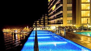 A swimming pool with a blue LED light strip, surrounded by lounge chairs and a building with multiple balconies. - Haytt-h2 Bocagrande Cartagena condominium (Cartagena)