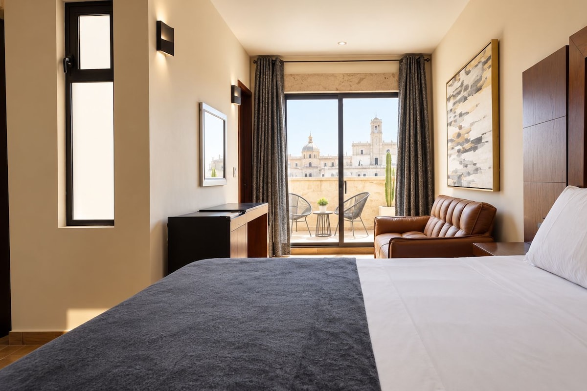 Une chambre d’hôtel avec un grand lit, un bureau, une chaise et une vue sur le paysage urbain par la fenêtre.