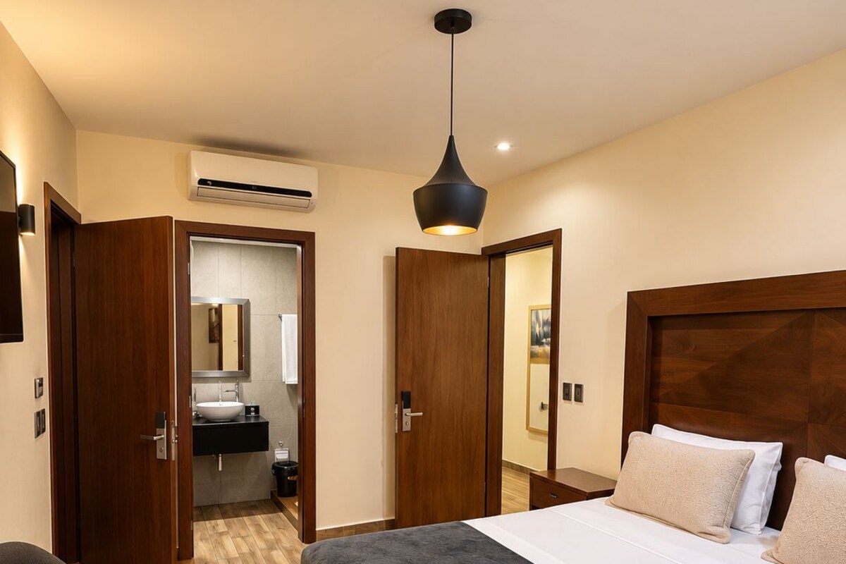 Une chambre d’hôtel comprenant un lit, des tables de chevet, un bureau, une chaise, une armoire, un miroir et un appareil de climatisation.