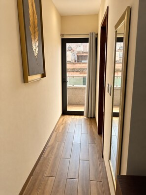 A hallway with a wooden floor, a door leading to a balcony, and a framed picture on the wall.