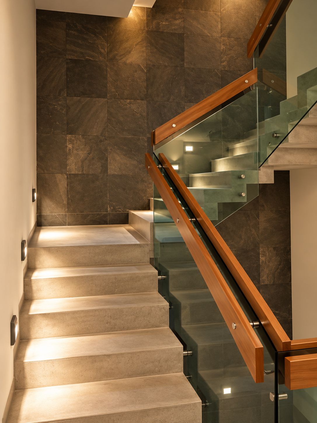 A modern staircase with glass railings and wooden handrails, leading to a lower level.