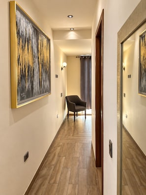 Un couloir avec un plancher en bois, une chaise et un tableau accroché au mur.