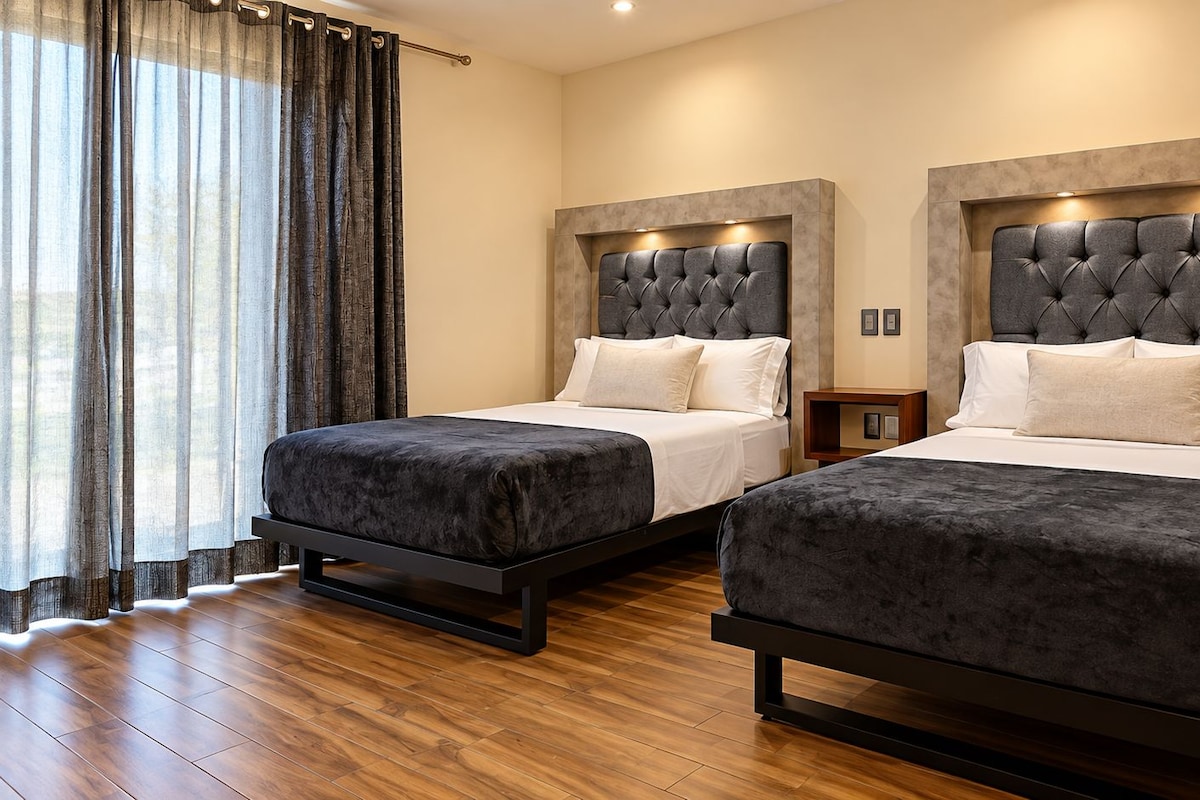 Une chambre d’hôtel avec deux lits, un plancher en bois et une grande fenêtre avec des rideaux.