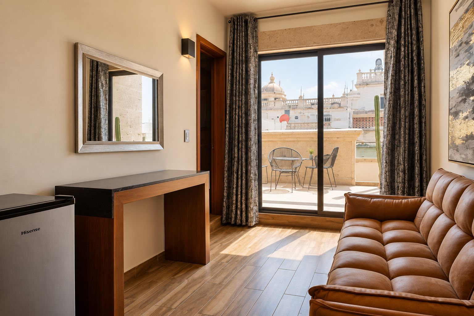 Ein möbliertes Zimmer mit Schreibtisch, einer Couch, einem großen Fenster mit Vorhängen und Blick auf Gebäude.