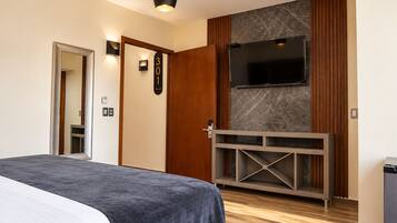 Ett hotellrum med en säng, en tv som är monterad på väggen, en trädörr och ett litet skåp.